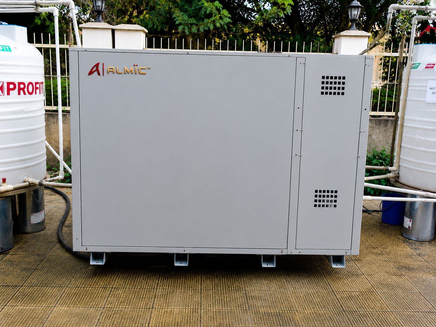ALMIC Ultra-Low Ambient Heat Pump unit installed outdoors beside hot water storage tanks